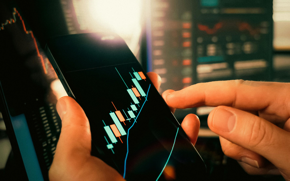 Close-up of hands using a smartphone displaying financial charts and analytics data.
